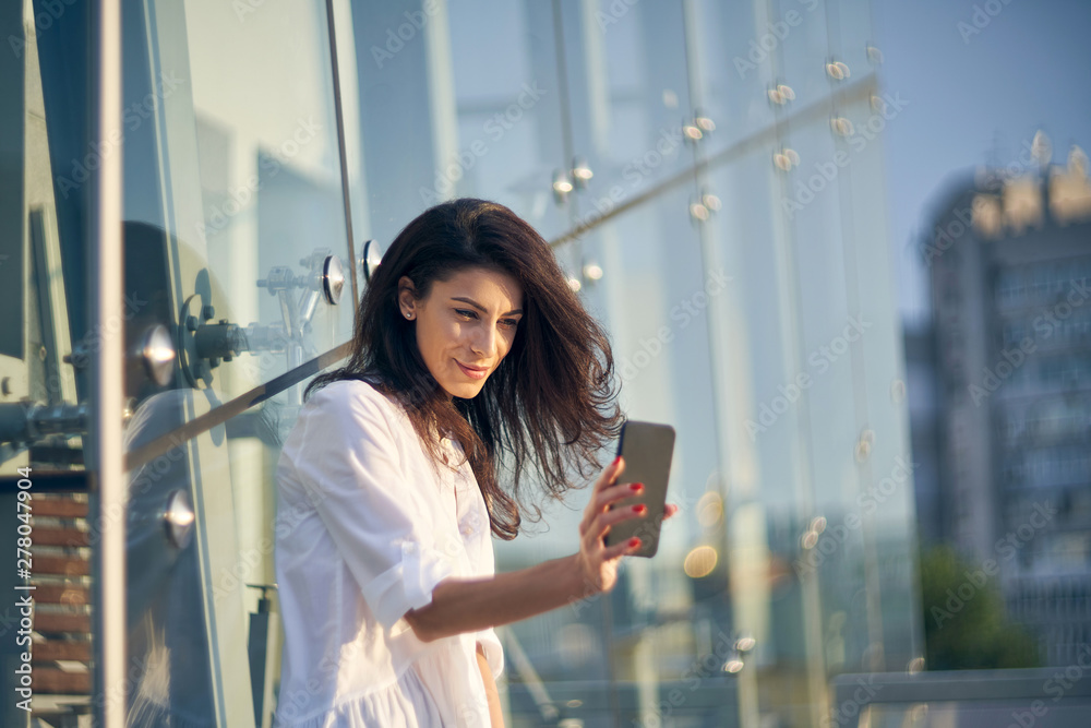 Woman making self portrait with her smart phone over modern office buiding