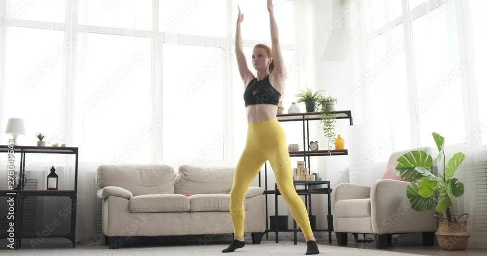 Fit woman doing jumping jacks exercise at home