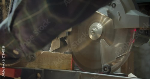 Close-up shot of hands of male senior carpenter carving the wood with headsaw into small squares at manufacture. photo