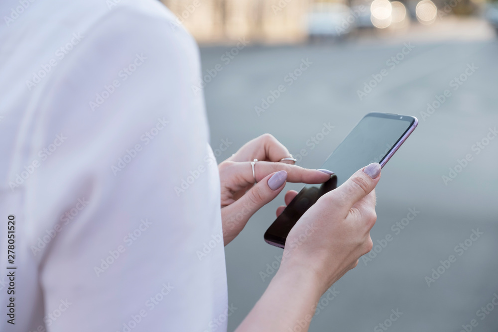 Beautiful brunette business woman in white skirt and grey suit trousers working on a mobile phone in her hands outdoors. European city on background. copy space Beautiful brunette business woman in white skirt and grey suit trousers working on a mobile phone in her hands outdoors. European city on background. copy space