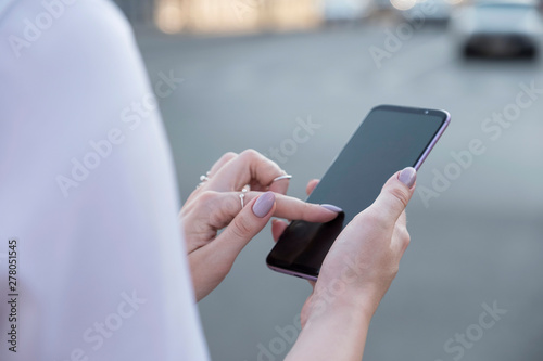 Beautiful brunette business woman in white skirt and grey suit trousers working on a mobile phone in her hands outdoors. European city on background. copy space © AnnaDemy
