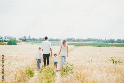 A family of four is walking in a wheat field on summer day.