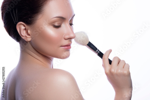 Cute brunette woman with natural make up. Clean flawless fresh skin. Close up beauty concept of skincare. She holds make up brush in her hand
