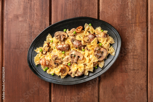Mushroom and cheese pasta. Farfalle with cremini and green peas, shot from above on a dark rustic wooden background