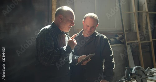 Two carpentry masters standing in the wood manufacture discussing the working plan in tablet. photo