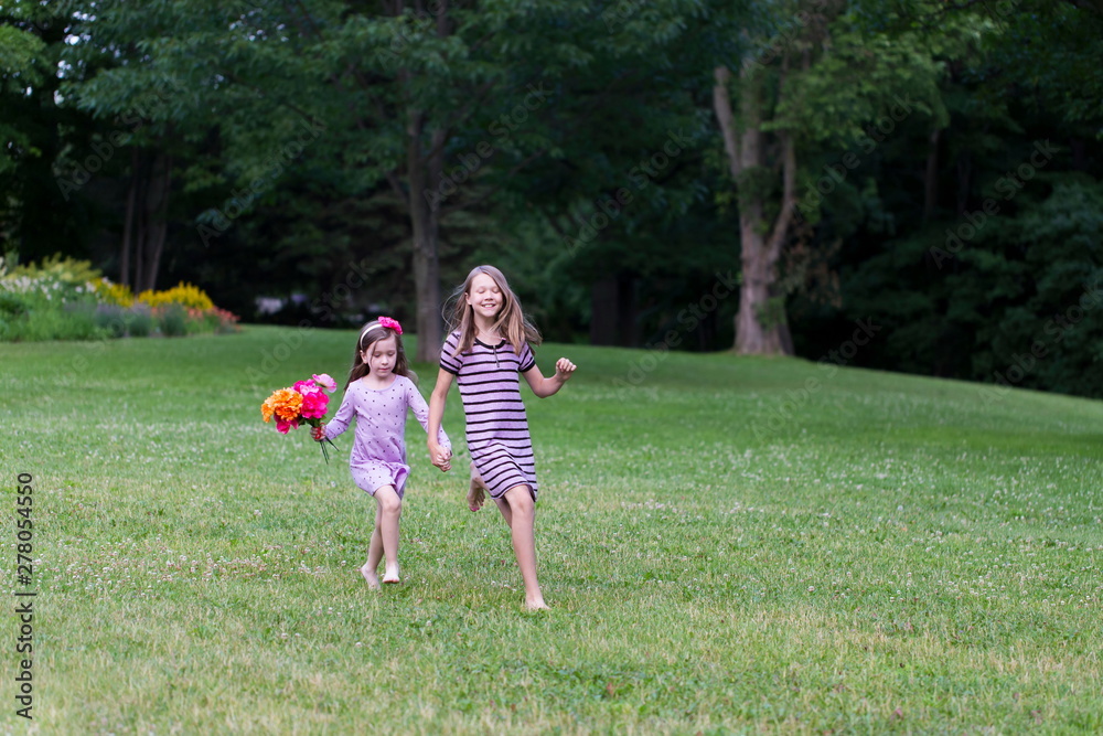 Naklejka premium Horizontal full length view of cute fair pre-teenager running in lawn with a small girl