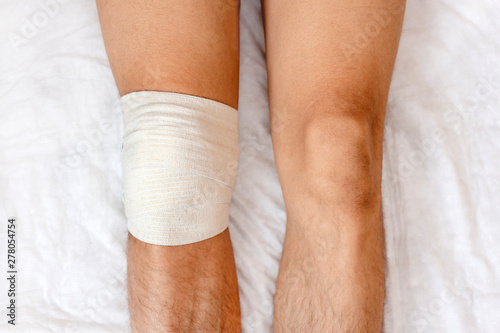 Man legs with gauze bandage in hospital office. Joint aspiration on knee, trauma. Limbs of patient. Health care and medicine concept. First aid. photo