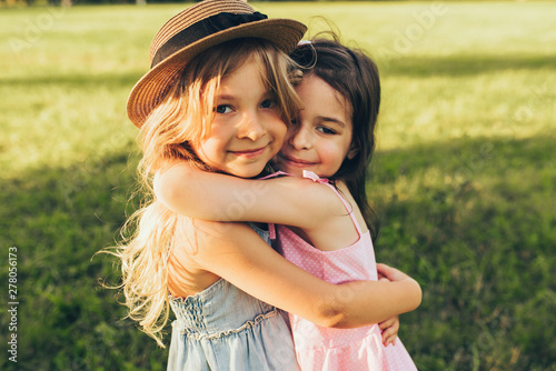 Outdoors portrait of two adorable children shares love and frienship. Two little girls playing in the park. Two sisters having fun on sunlight and nature background. Childhood and friendship concept