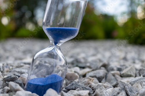 Hourglass with beautiful blue sand lie on small stones