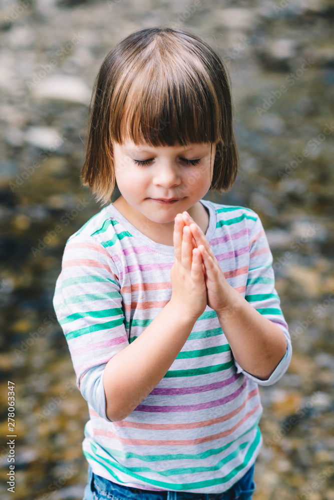 Little girl praying with eyes closed on the shore of a mountain stream Little girl praying with eyes closed on the shore of a mountain stream