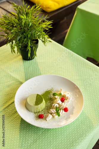 Smooth matcha panna cotta with whipped cream cheese and cherry, powdered with matcha tea and served on a green terrace