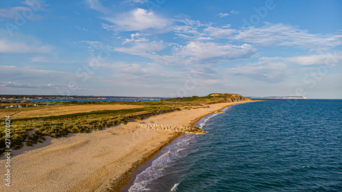 An aerial view of a beautiful sandy beach along blue water sea and amaizing cliffs in the background at golden hour under a majestic blue sky and white clouds