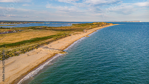 An aerial view of a beautiful sandy beach along blue water sea and amaizing cliffs in the background at golden hour under a majestic blue sky and white clouds