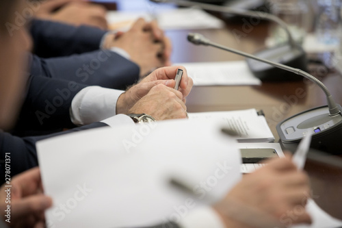 A politician or businessman in a suit sits at a polished wooden table in front of a microphone during a discussion, duty, or presentation. Without a face. photo