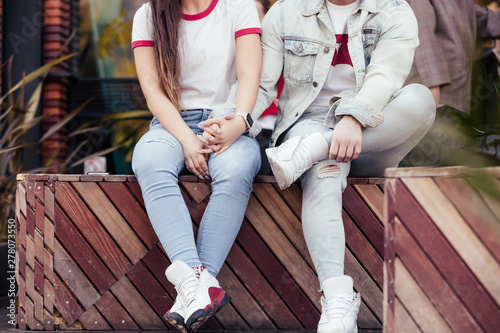 Unidentified young married couple is a stylish guy and a girl holding hands sitting on a bench and booking a hotel using a smartphone and high-speed Internet. Online shopping concept