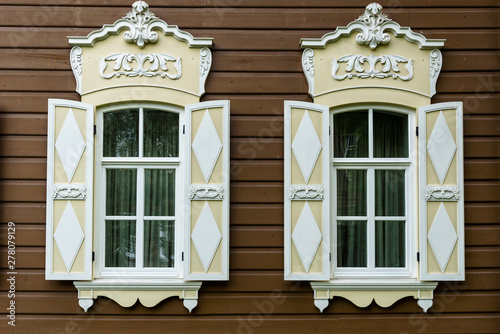 two windows with the wooden carved architrave in the old wooden house in the old Russian town. photo