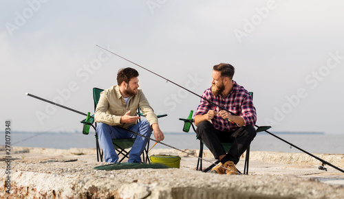 leisure and people concept - friends or fishermen adjusting fishing rods with bait on pier