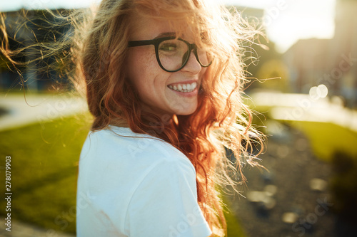 Portraits of a charming red-haired girl with a cute face. Girl posing for the camera in the city center. She has a wonderful mood and a lovely smile photo