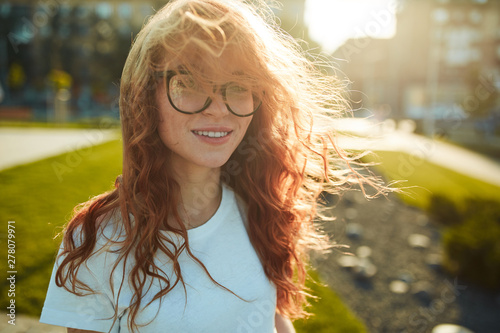 Portraits of a charming red-haired girl with a cute face. Girl posing for the camera in the city center. She has a wonderful mood and a lovely smile