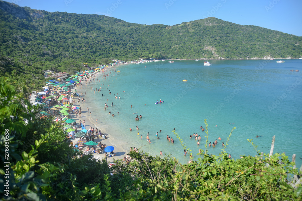 Playa tropical brasileña con agua turquesa y cristalina entre montañas con gente. 