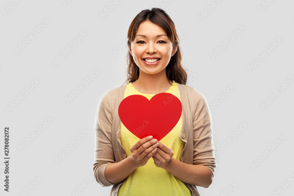love, valentine's day and charity concept - happy asian young woman with red heart over grey background
