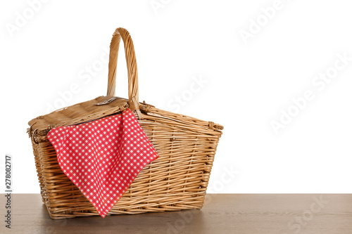 Closed wicker picnic basket with checkered tablecloth on wooden table against white background