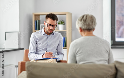 geriatric psychology, mental therapy and old age concept - senior woman patient and psychologist with clipboard taking notes at psychotherapy session