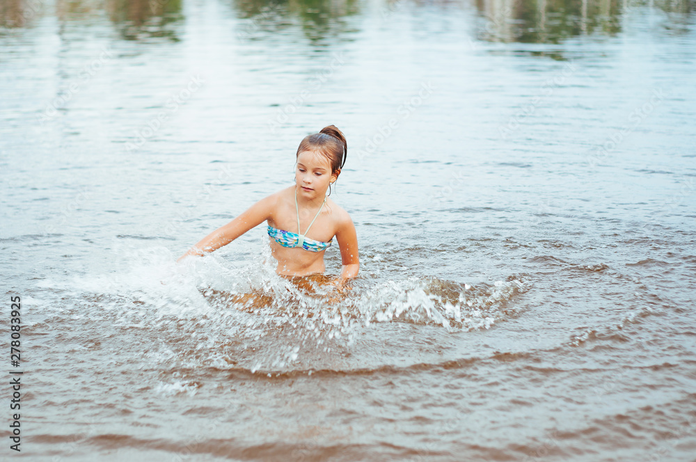 Fototapeta premium Little happy girl plays with water and splashes of water in the sea