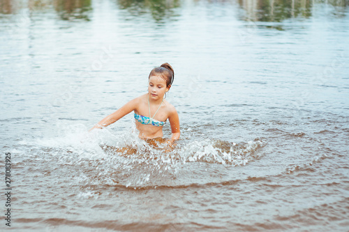 Little happy girl plays with water and splashes of water in the sea