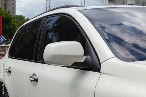 Close-up of the side left mirror with window of the car body white SUV on the street parking after washing and detailing in auto service industry. Road safety while driving