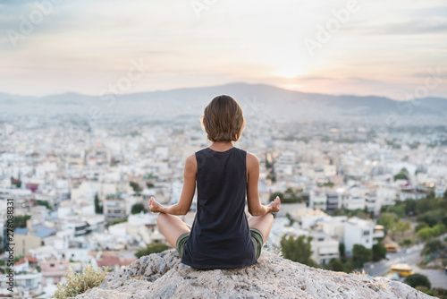 Young woman practicing yoga outdoors at sunset with a big city at the background. Harmony, meditation and healthy lifestyle concept © kite_rin