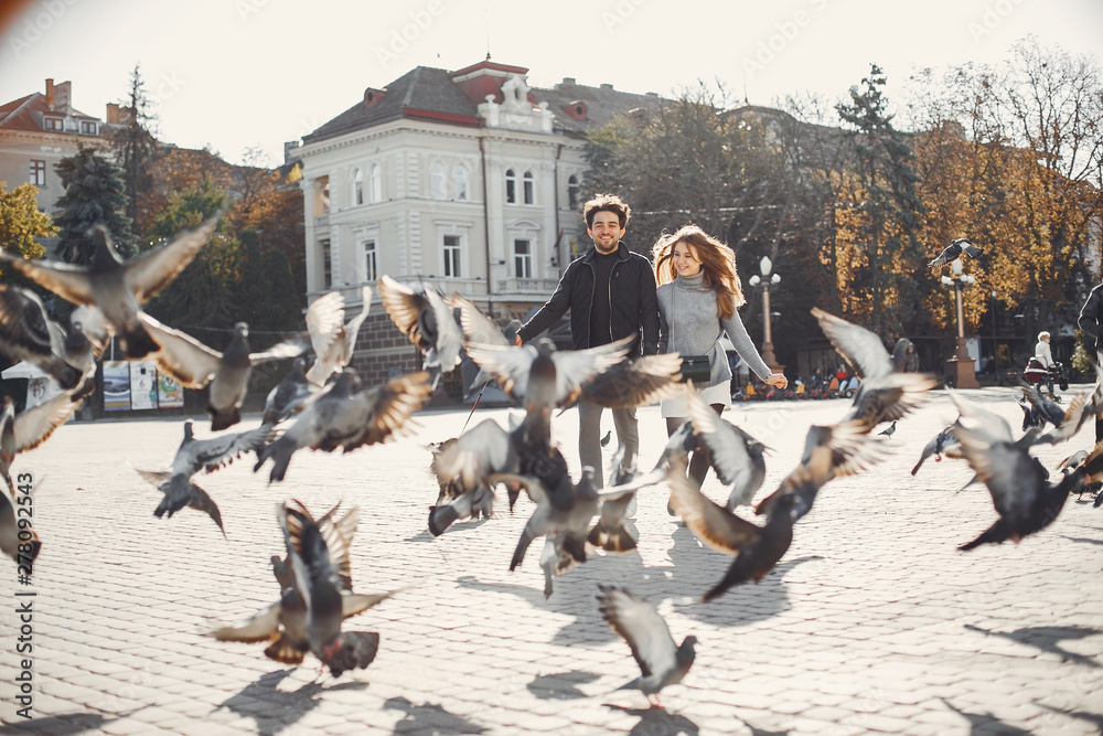 Obraz premium Cute couple in a spring city. Lady with long hair. Man in a black jacket. Two people with a dog