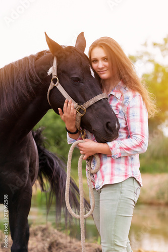 young woman standing outdoors with her black horse