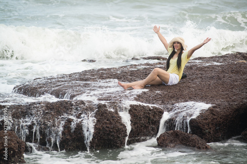 Asian pretty female sitting on rocks with strong wave and relaxation happiness.