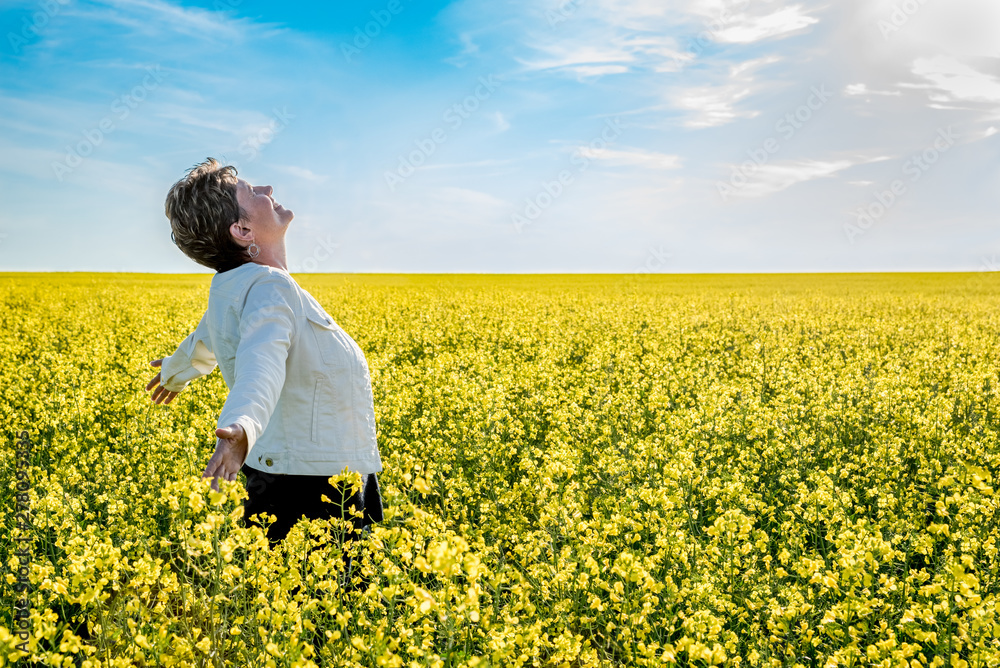 Young caucasian woman standing with arms raised in a canola field in bloom Young caucasian woman standing with arms raised in a canola field in bloom