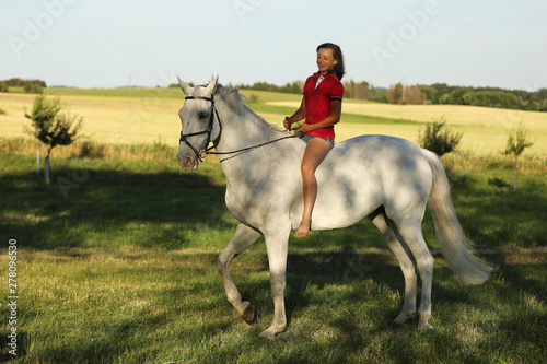 Teen girl ride on white horse without saddle on meadow in late afternoon © sci