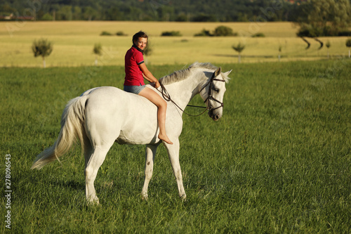 Young girl ride on white horse without saddle on meadow in late afternoon, sunset time © sci