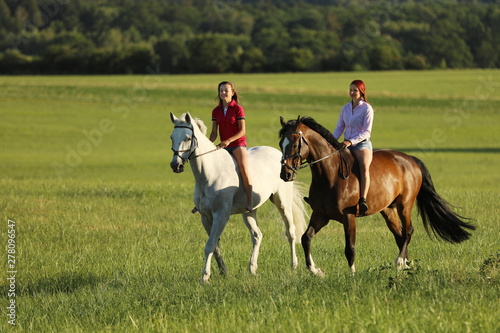 Couple of girls on horses walking through summer nature in the afternoon time