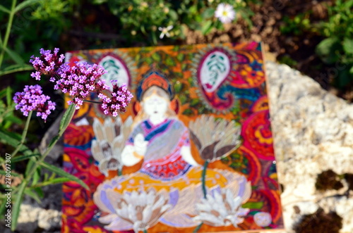 Hand painted stained glass picture with Buddha on it. Stone and flower background,