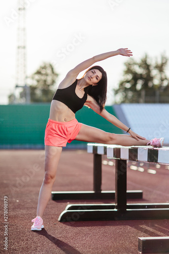 Obraz na płótnie Beautiful brunette runner woman doing stretching leaning her leg on barrier for running stretching before workout - outdoor shot. Sport girl doing exercise in the stadium w salonie