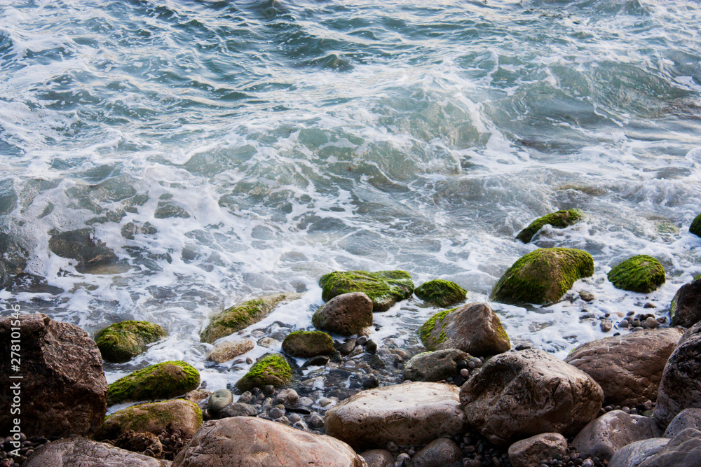 Stone beach of the Black Sea with magnificent waves of the surf. View of the surf waves on the sea beach on a summer day. Foam from the surf on the stones close-up. Stone beach of the Black Sea with magnificent waves of the surf. View of the surf waves on the sea beach on a summer day. Foam from the surf on the stones close-up.