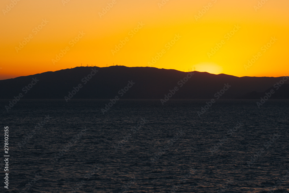 Sun setting behind the profile of an island carpeted with wind turbines