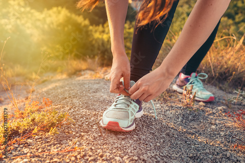 Woman tying shoelaces on sneakers. The sun shines on the left. The concept of sports lifestyle and training. The appearance of the feet and hands