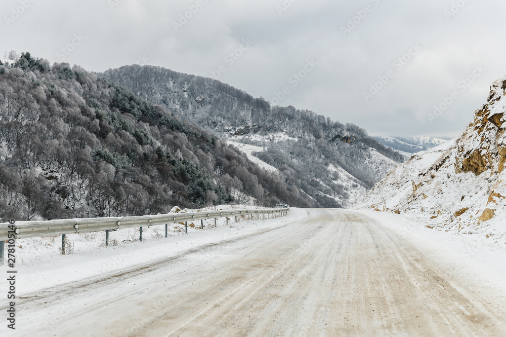 Empty mountain asphalt road in winter covered with snow on a cloudy day. The concept of driving a car in winter ice and travel