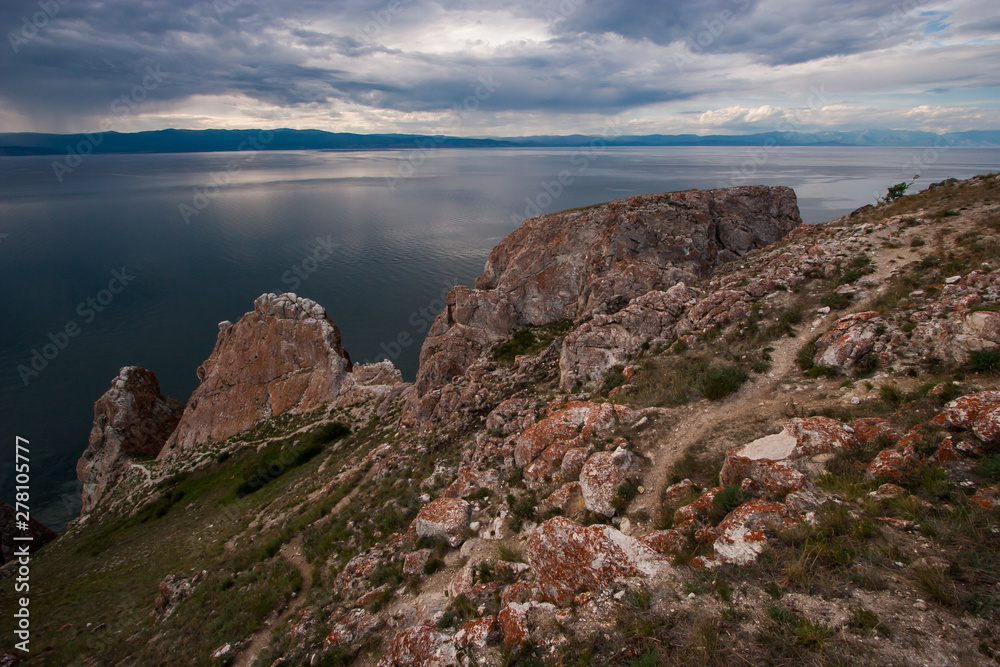 Three Brothers Rocks on Olkhon Island on Lake Baikal. Behind the mountain lake. The sky with clouds. It rains over the mountains. In the water, a beautiful reflection of the sky.