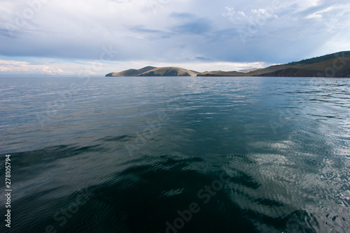 Beautiful view of the water of Lake Baikal per day with clouds in the sky. View from the water. The water is green. On the horizon are hills.