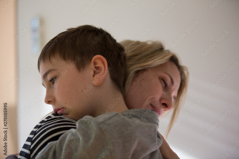 Blonde mother and brunette boy hug each-other warm. Indoor, natural light. Blonde mother and brunette boy hug each-other warm. Indoor, natural light.