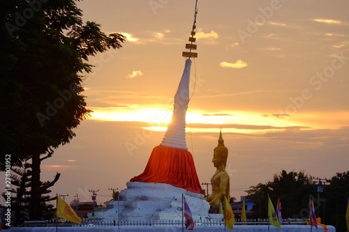 A white ancient pagoda beside a river at Kohkret,Nonthaburi with silhouette sunset over the bright sky at dusk and a large golden sitting statue background photo