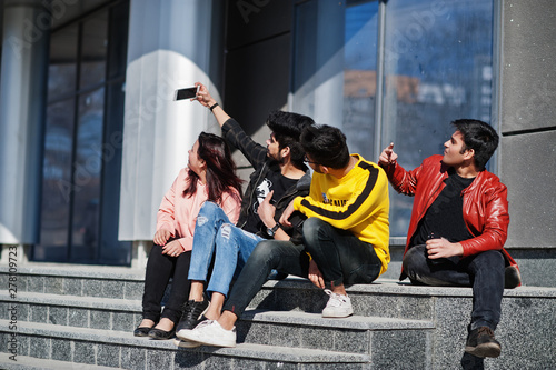Group of asian people friends sitting on stairs outdoor against modern building and making selfie by phone.