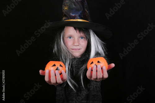 happy laughing child girl in witch costume with Halloween pumpkin candy jar on black background